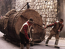 Un grande tronco di legno trainato da due uomini in costume 