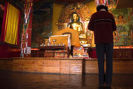 Un giovane in raccoglimento davanti alla statua di Buddha. 